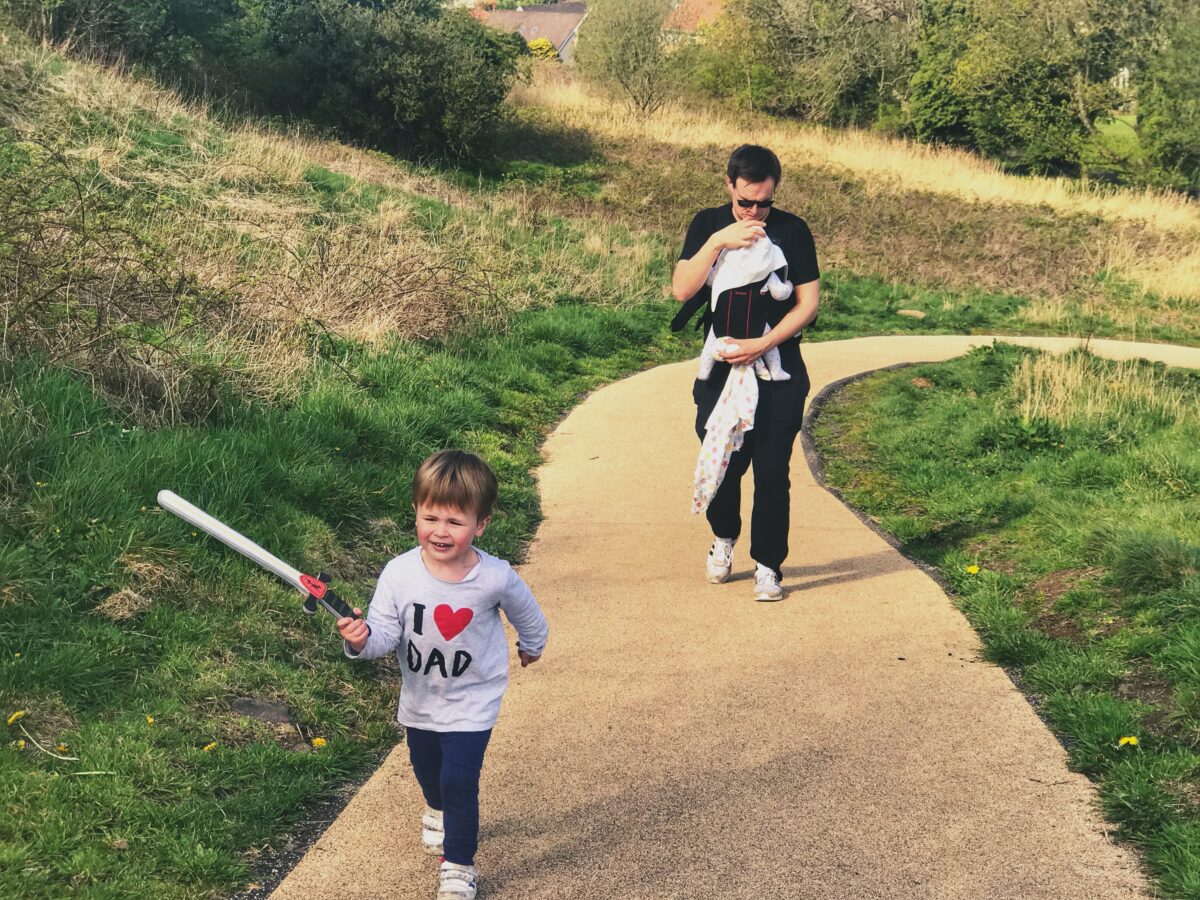 Neil, cary baby Felix and Dexter, carrying a plastic sword walking up the beige path to Dundonald castle